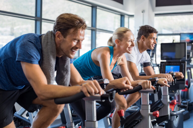 Group,Of,Smiling,Friends,At,Gym,Exercising,On,Stationary,Bike